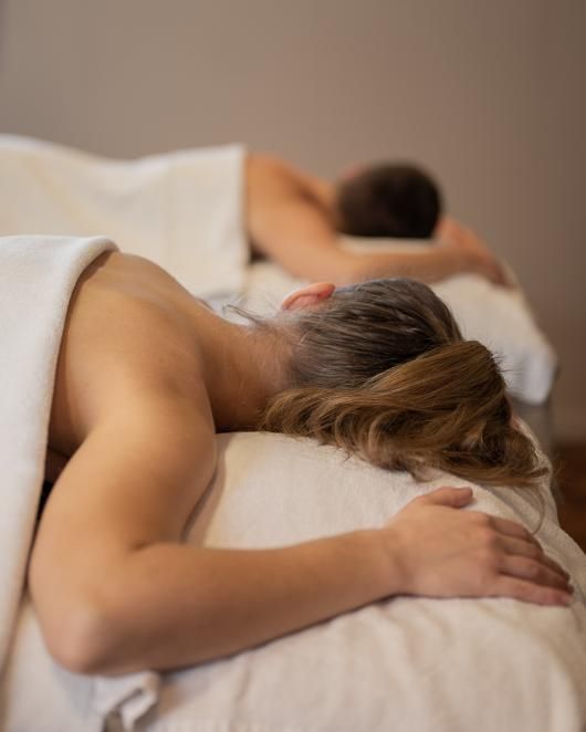 Deux personnes allongées face contre terre sur des tables de massage dans une salle de soins d'un spa