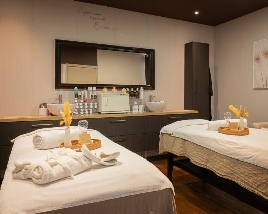 Salle de soins spa avec deux tables de massage, serviettes et produits de soin sur un comptoir en bois