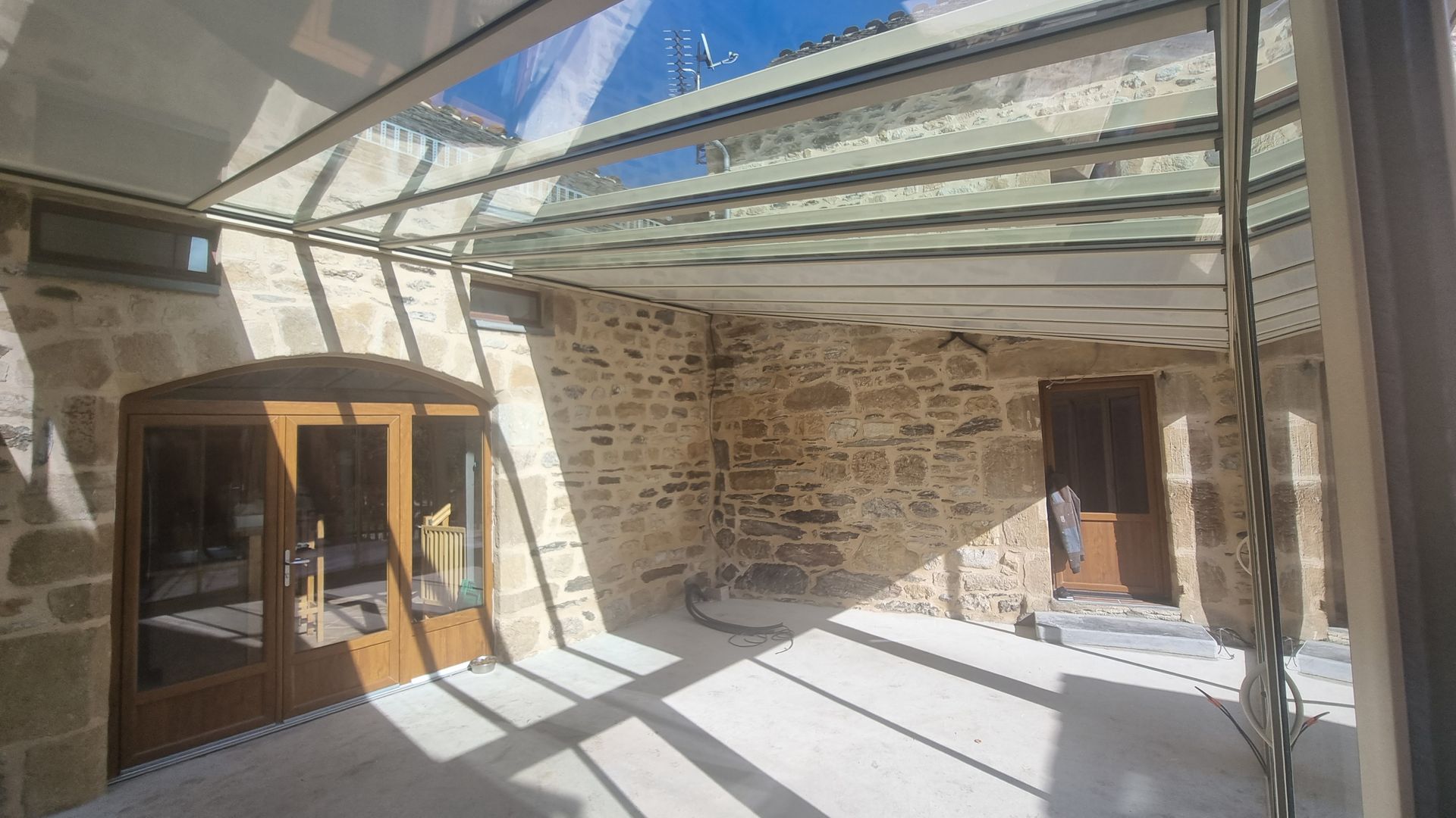 Une cour intérieure avec des murs en pierre apparente, un sol pavé clair et un toit en verre rétractable moderne.
