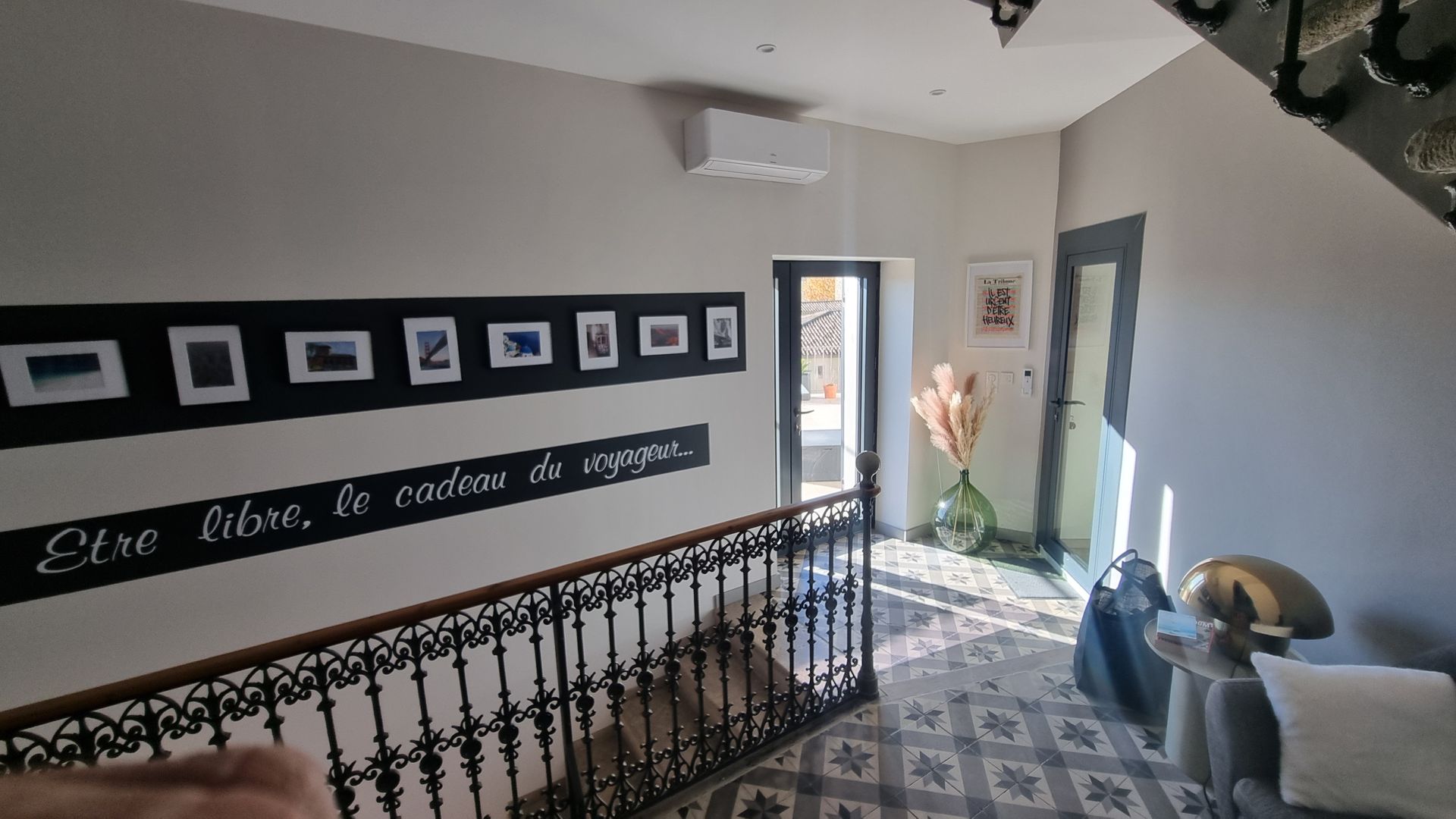 Le couloir est agrémenté d'une rampe en fer forgé, de carreaux de sol décoratifs, de photos encadrées au mur et d'un climatiseur.