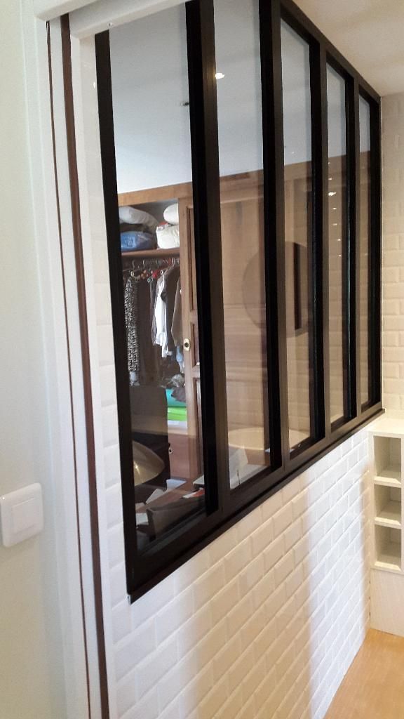 Une cloison intérieure en verre à cadre métallique noir, placée au-dessus d'un muret en carrelage métro blanc.