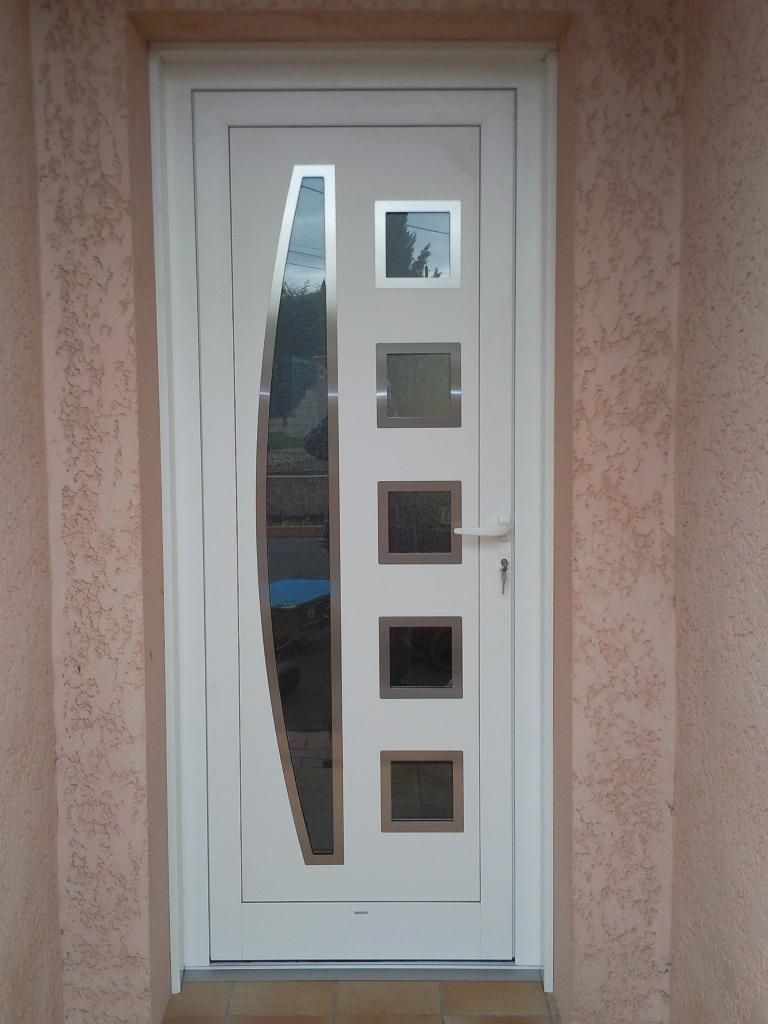 Porte d'entrée blanche avec une fenêtre verticale incurvée à gauche et cinq panneaux de verre carrés disposés en colonne à droite.