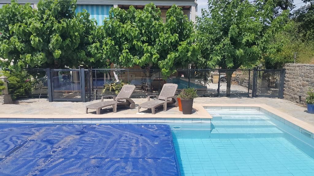 Une piscine avec une couverture bleue, à côté de deux chaises longues sur une terrasse avec des arbres et un bâtiment en arrière-plan.