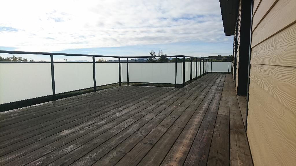 Une terrasse en bois avec une rambarde en métal noir et des panneaux de verre dépoli se détachant sur un fond de ciel.