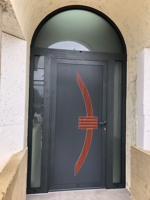Porte d'entrée moderne gris foncé avec un élément décoratif orange incurvé et des fenêtres latérales, surmontée d'un panneau de verre arqué.