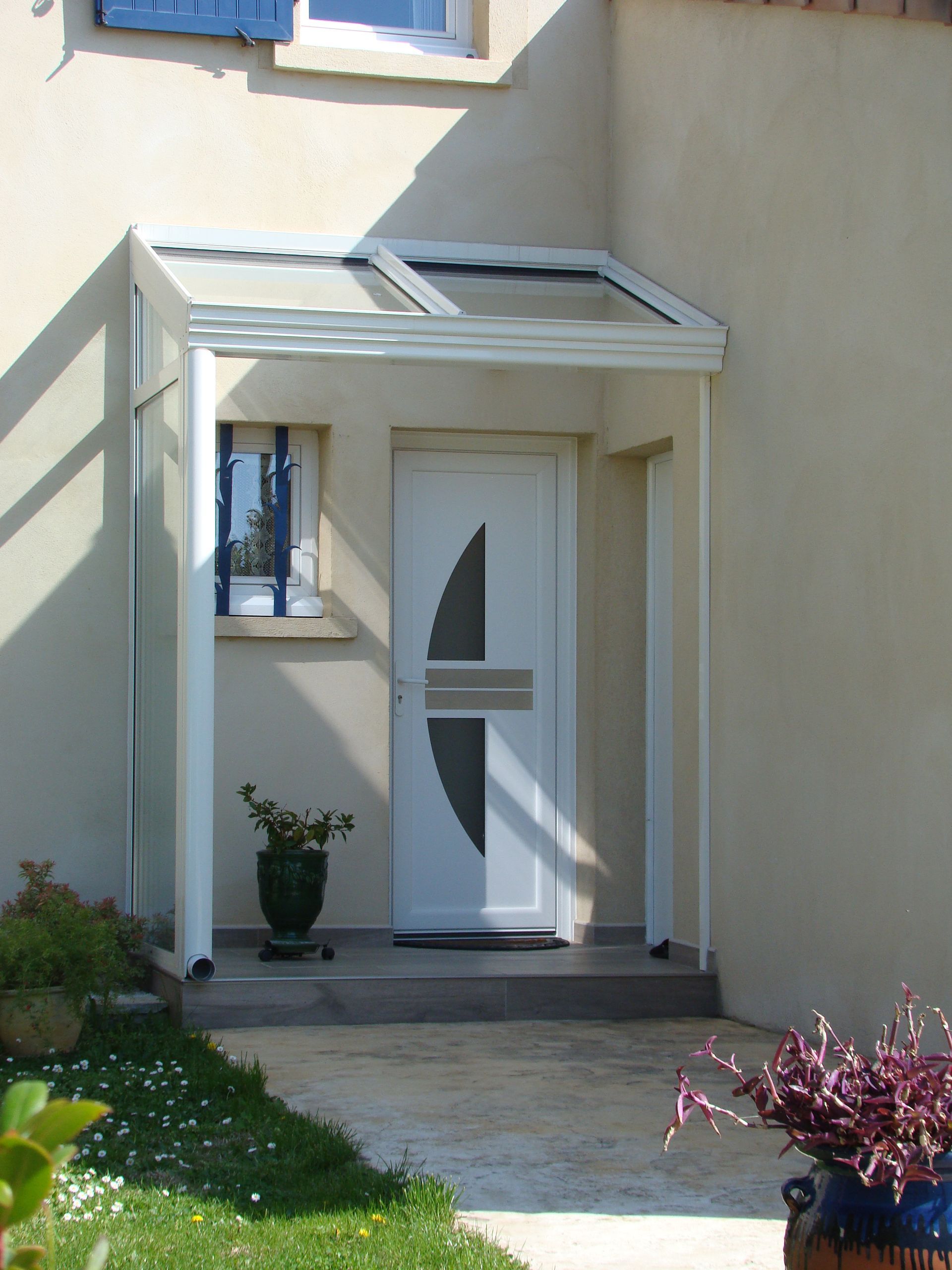 Une porte d'entrée blanche avec un porche moderne auvent vitré se détachant sur une façade beige.