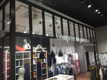 Une façade de magasin pour « Comptoir du pantalon », avec une structure en verre et en métal noir, des mannequins et des présentoirs à vêtements.