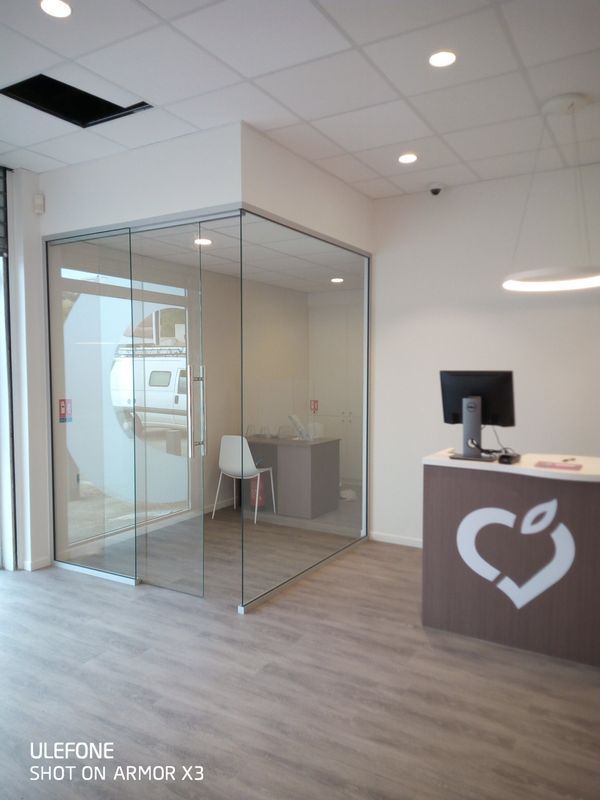 Un espace d'accueil avec un bureau blanc orné d'un logo en forme de cœur et un bureau vitré contenant un bureau et une chaise.