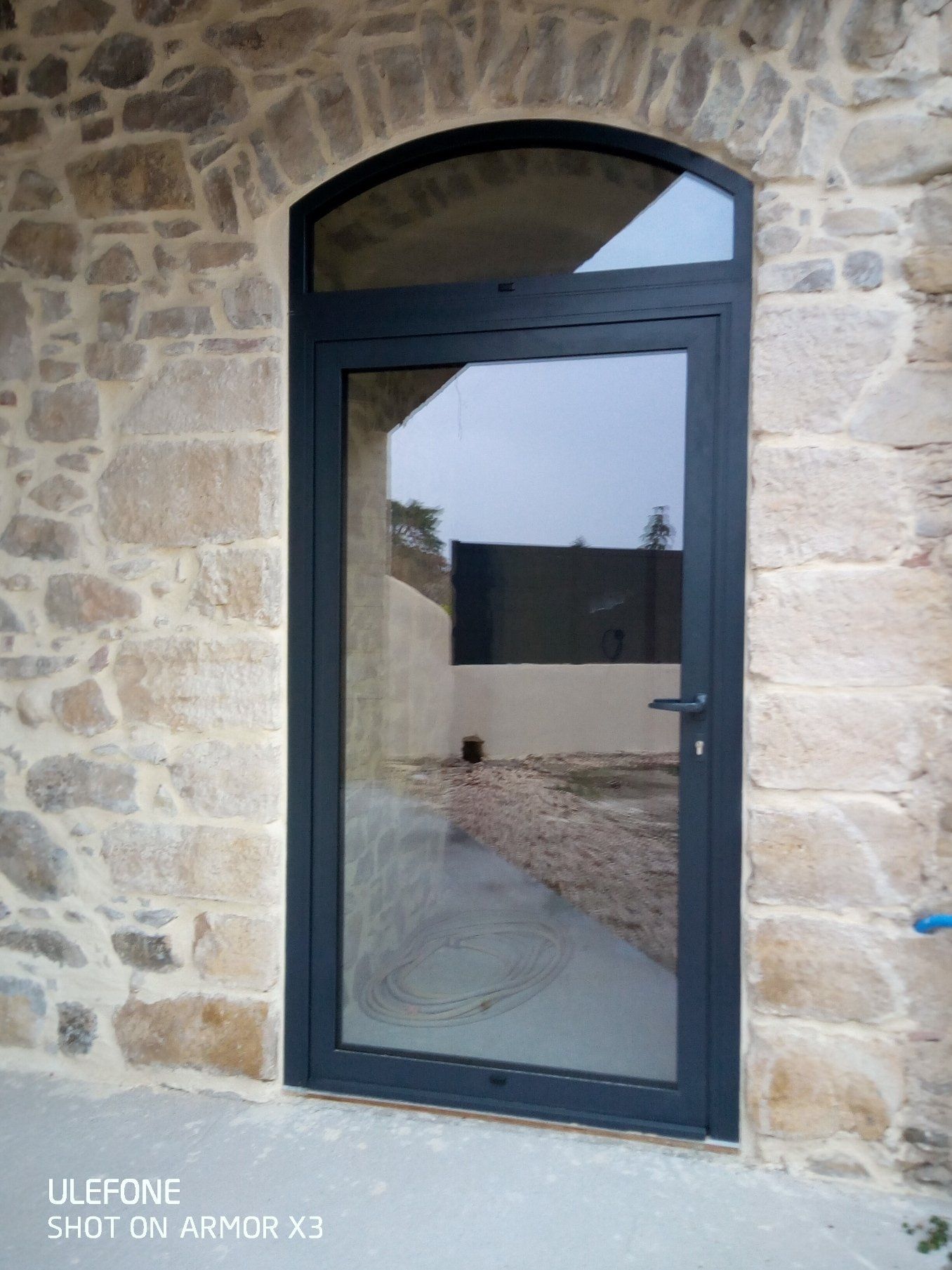 Une porte vitrée cintrée à cadre sombre, encastrée dans un mur de pierre rustique.