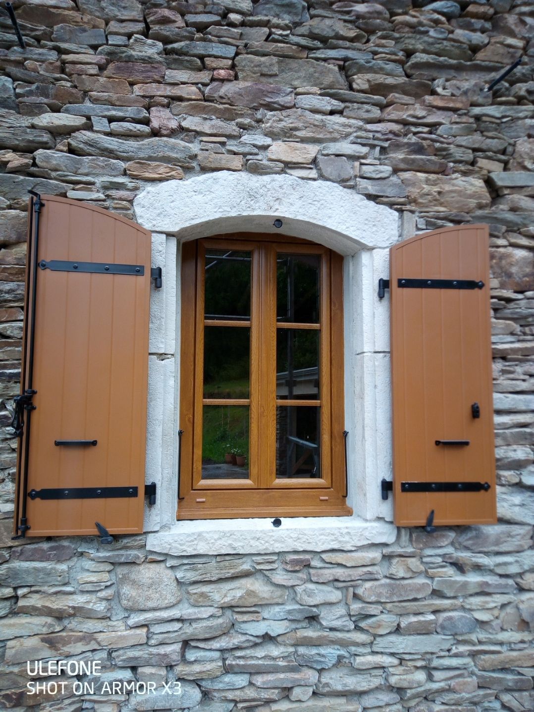 Une fenêtre en bois aux volets ouverts, encastrée dans un mur de pierre rustique.