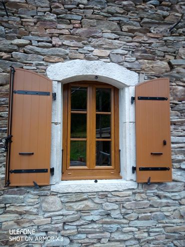 Une fenêtre à ossature bois avec des volets ouverts, encastrée dans un mur de pierre rustique.