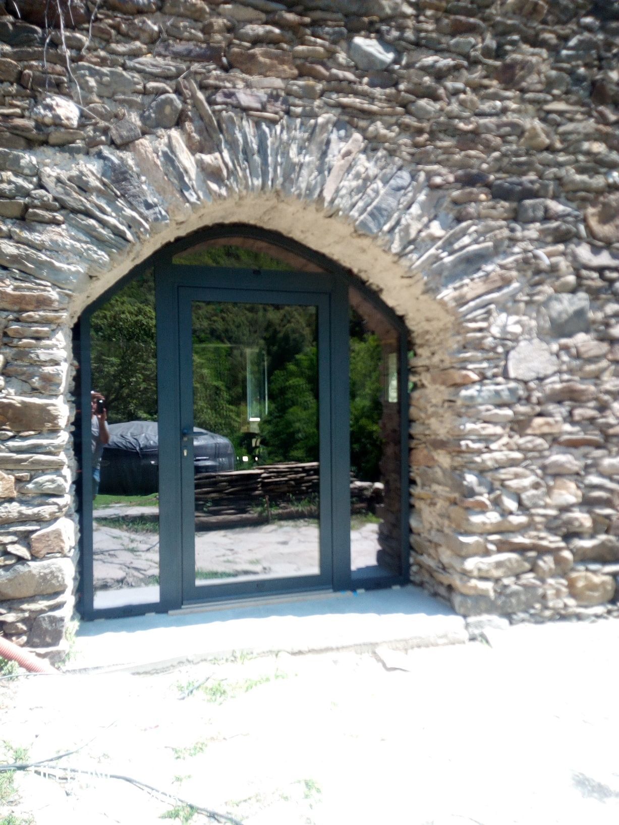 Une porte vitrée moderne à cadre sombre, intégrée à une entrée rustique en pierre voûtée.