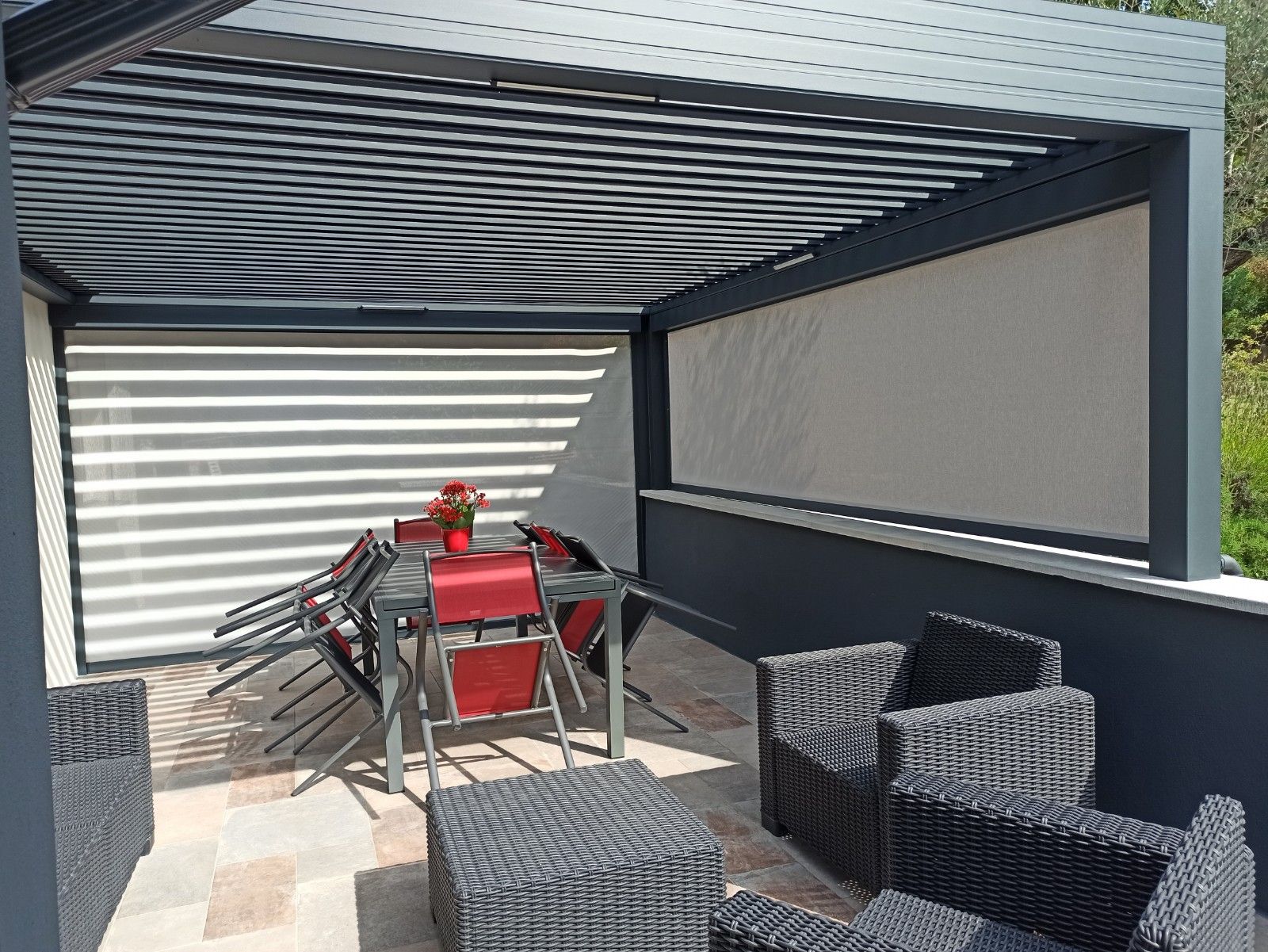 Une terrasse moderne avec une pergola à persiennes abritant une table et des chaises de salle à manger, adjacente à un coin salon avec des sièges en osier.