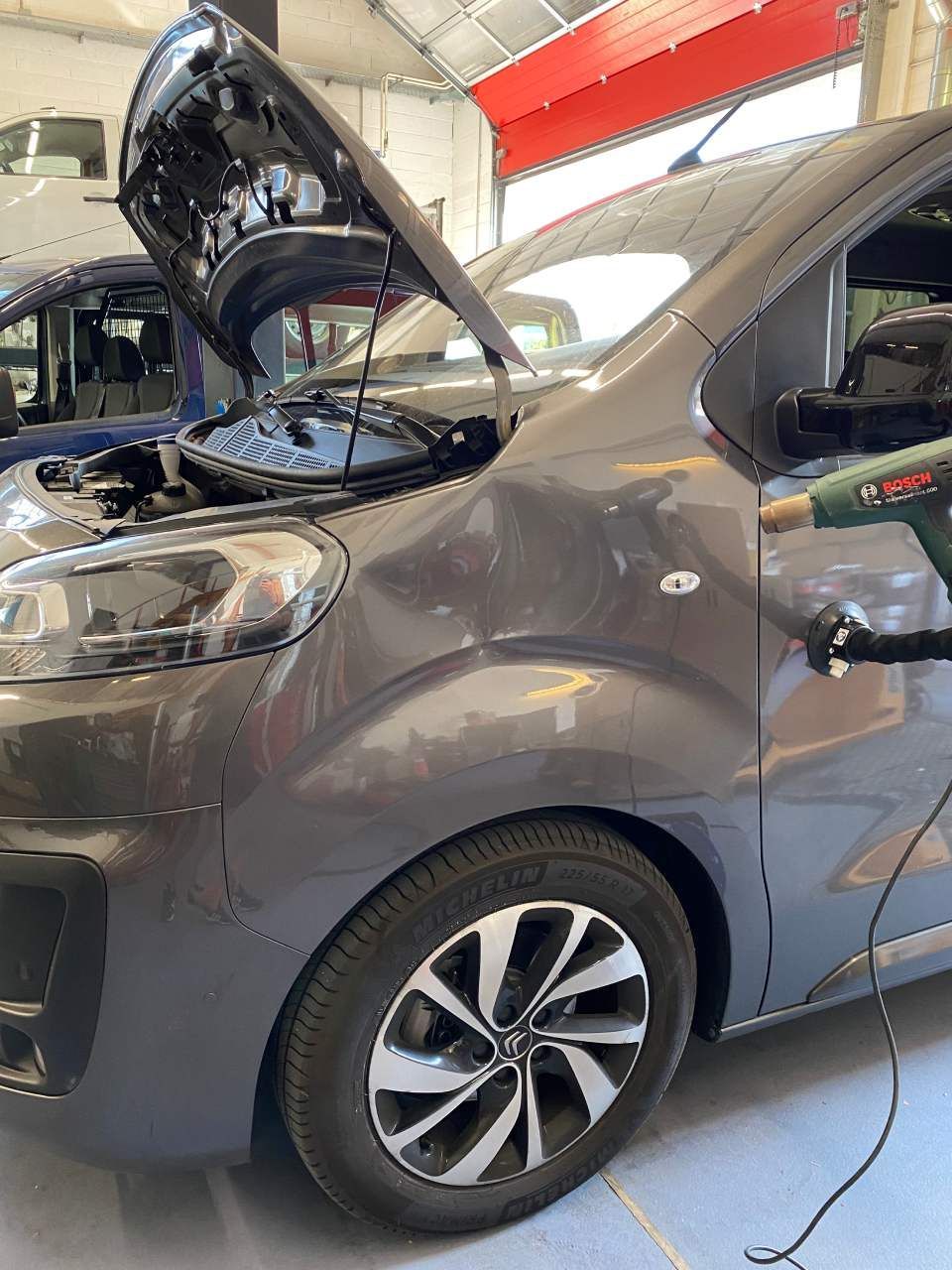 Une voiture avec son capot ouvert est en cours de réparation dans un garage.