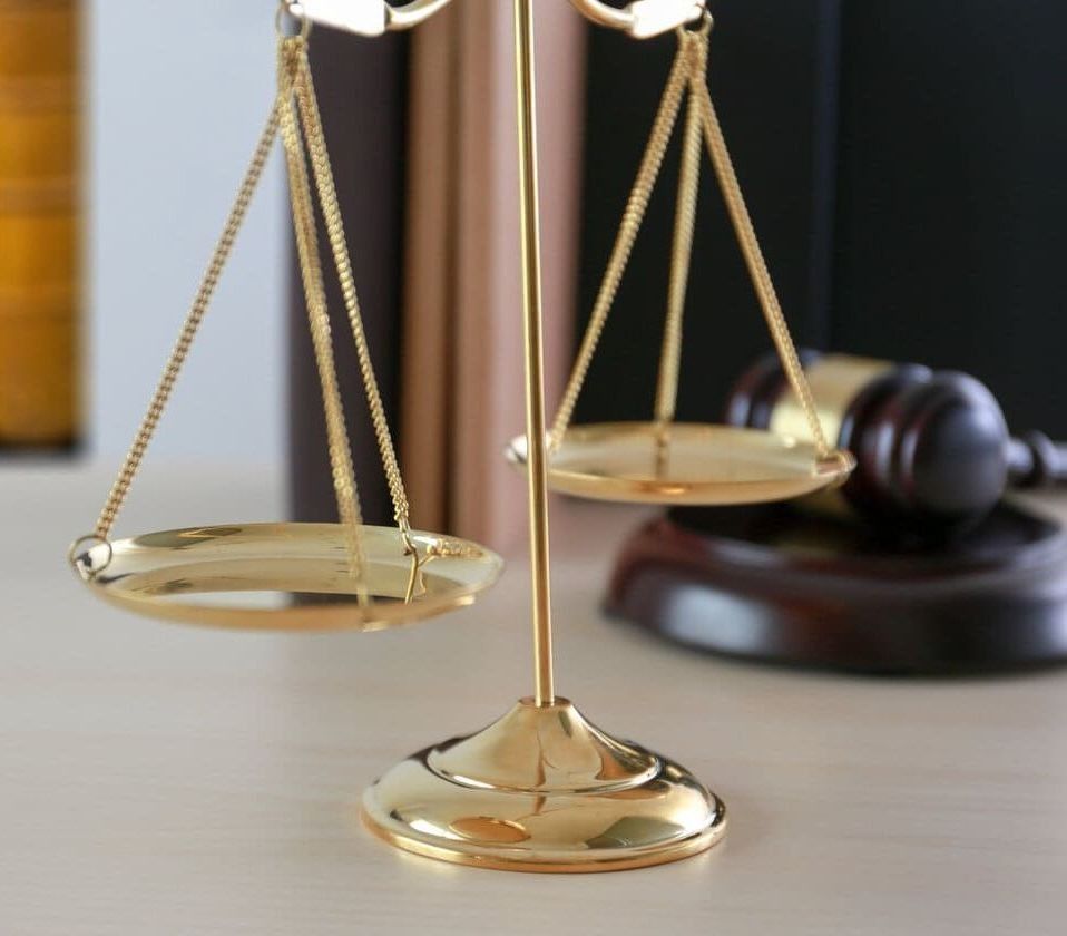 Balanza de la justicia de oro con un mazo y libros de leyes en el fondo.