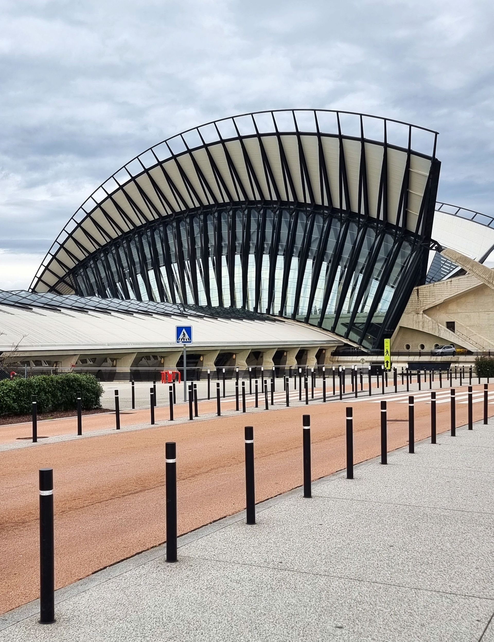Façade moderne et incurvée d’une gare, avec une verrière et une place pavée déserte à l’avant