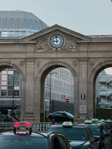Arche en pierre historique avec une horloge et de la circulation en dessous, des voitures circulant dans une rue de la ville.