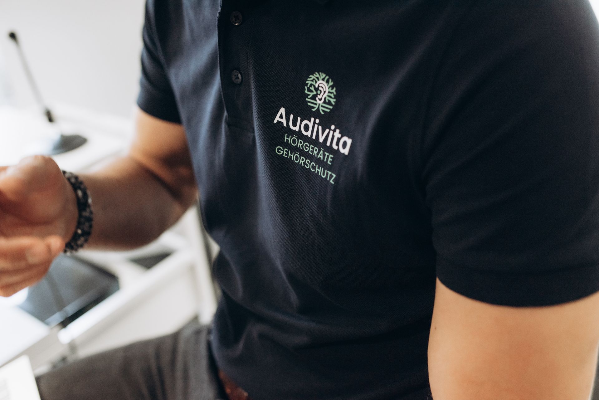 Ein Mann mit grauem Haar und Bart, der eine braune Jacke trägt, berührt sein Ohr und blickt zur Seite.