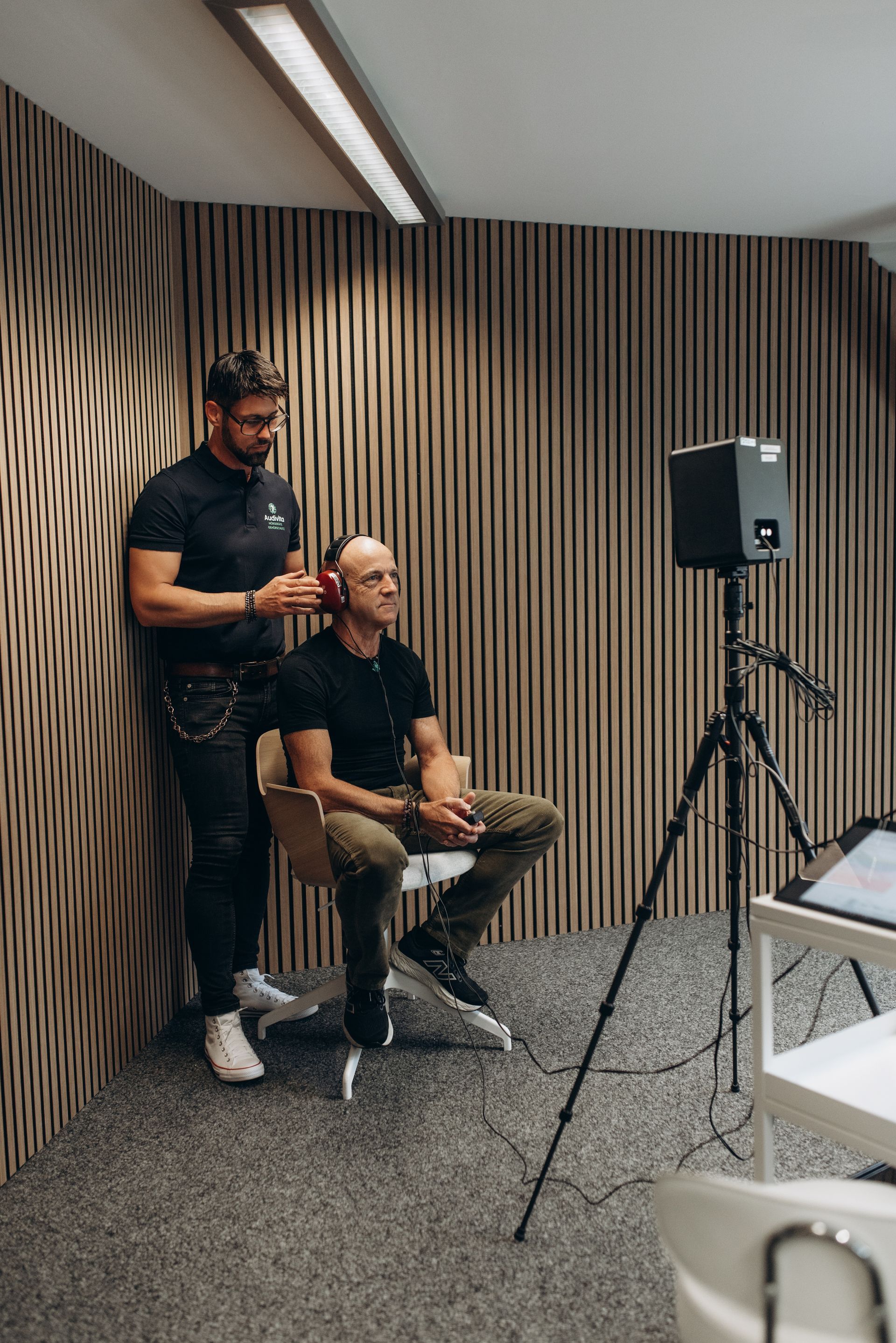 Mann und Frau posieren neben einem Auto, der Mann trägt eine Brille und einen Rollkragenpullover, die Frau ein schwarzes Top und Jeans, beide lächeln.