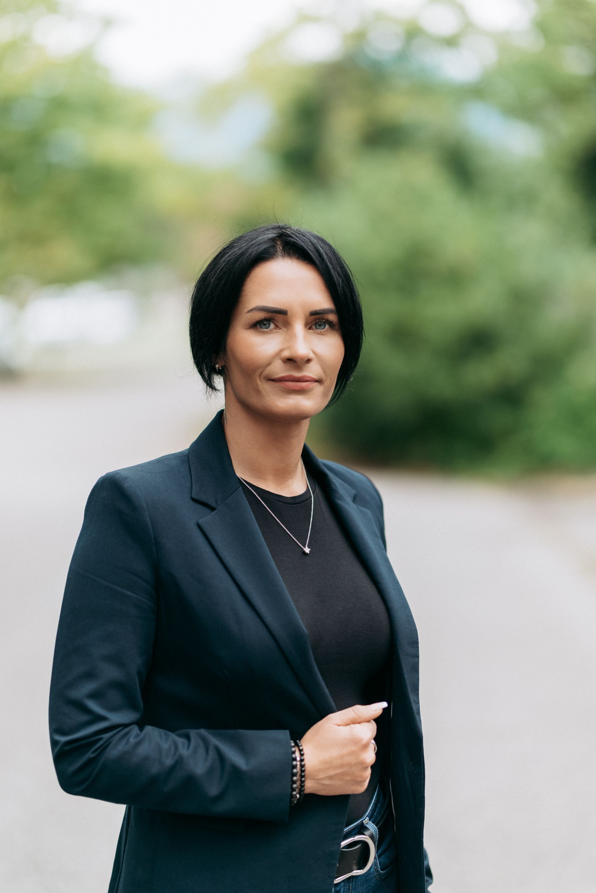 Mann und Frau posieren neben einem Auto, der Mann trägt eine Brille und einen Rollkragenpullover, die Frau ein schwarzes Top und Jeans, beide lächeln.