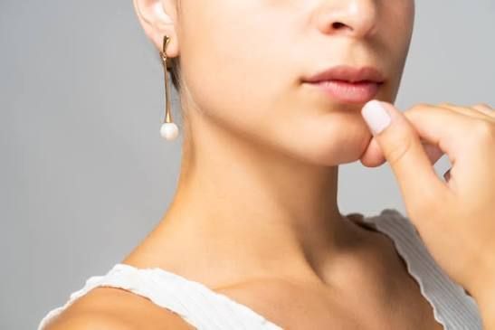 Mujer que lleva un pendiente de oro con una perla, sujetándose la barbilla.