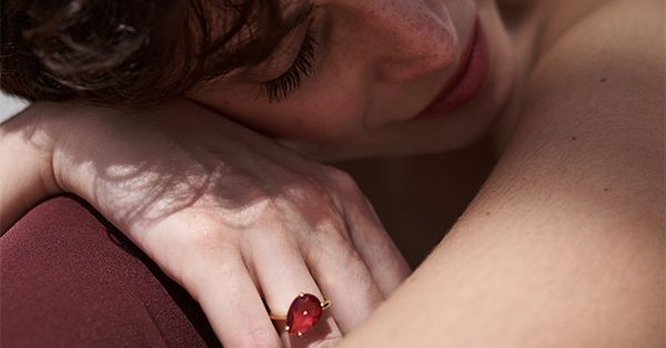 Persona con los ojos cerrados, apoyada en un hombro; lleva un gran anillo con una gema roja. Iluminación tenue.