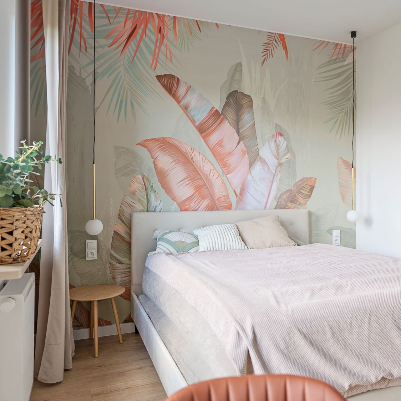 Une chambre avec un lit beige adossé à un mur d'accent à thème botanique orné de grandes feuilles tropicales couleur pêche.