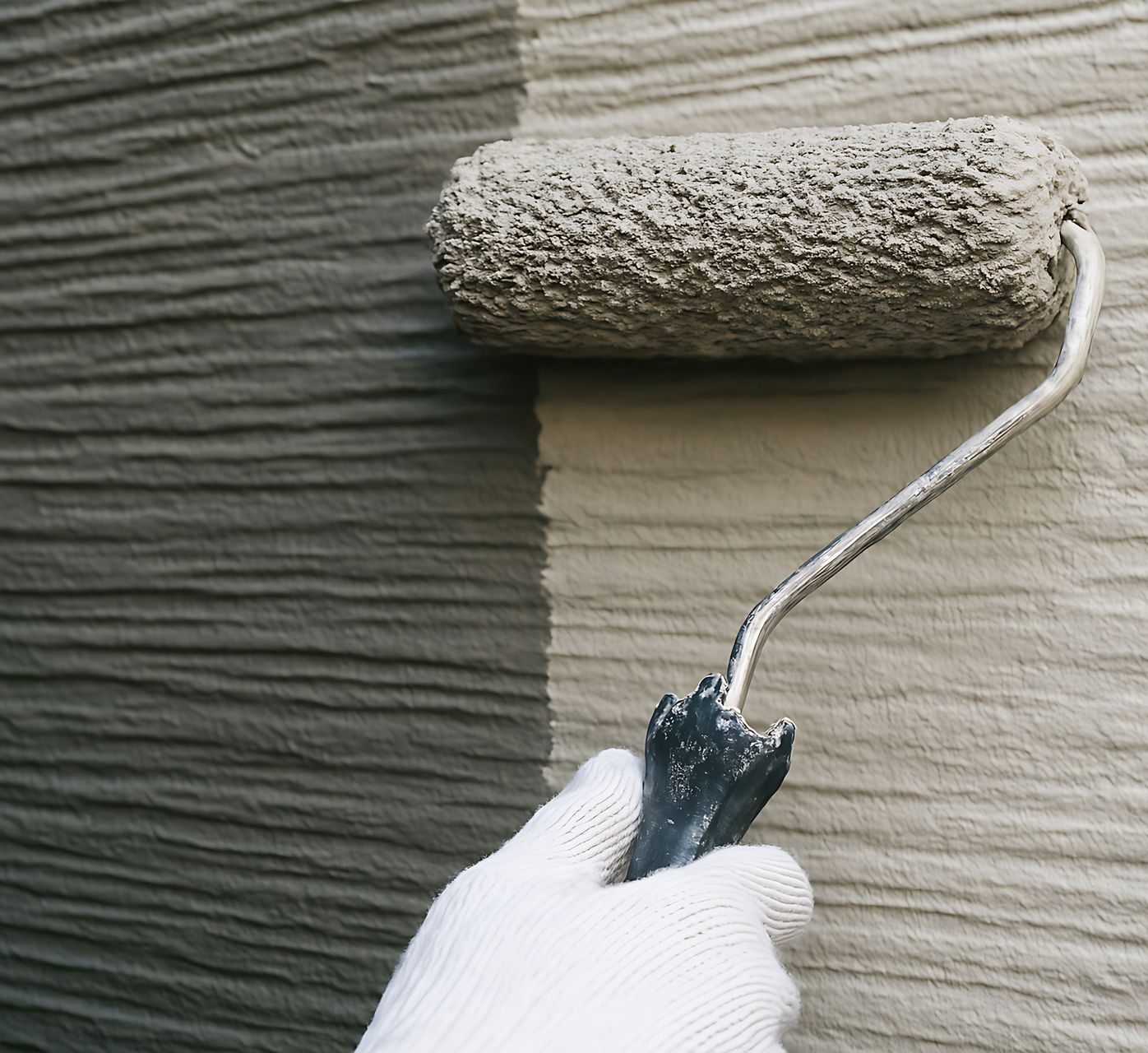 Un rouleau à peinture applique une peinture beige clair sur une surface texturée foncée.