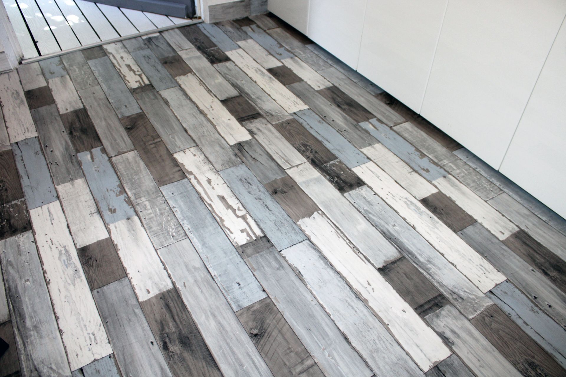 Revêtement de sol composé de planches de bois patinées dans différentes nuances de gris, de blanc et de brun, disposées en quinconce.