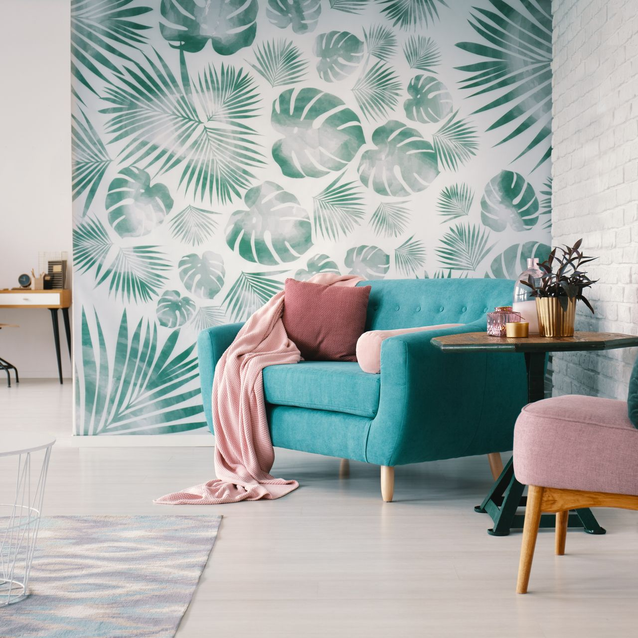 Une pièce lumineuse comprend un fauteuil turquoise avec un jeté rose, une petite table d'appoint et un mur orné de motifs de feuilles tropicales vertes.