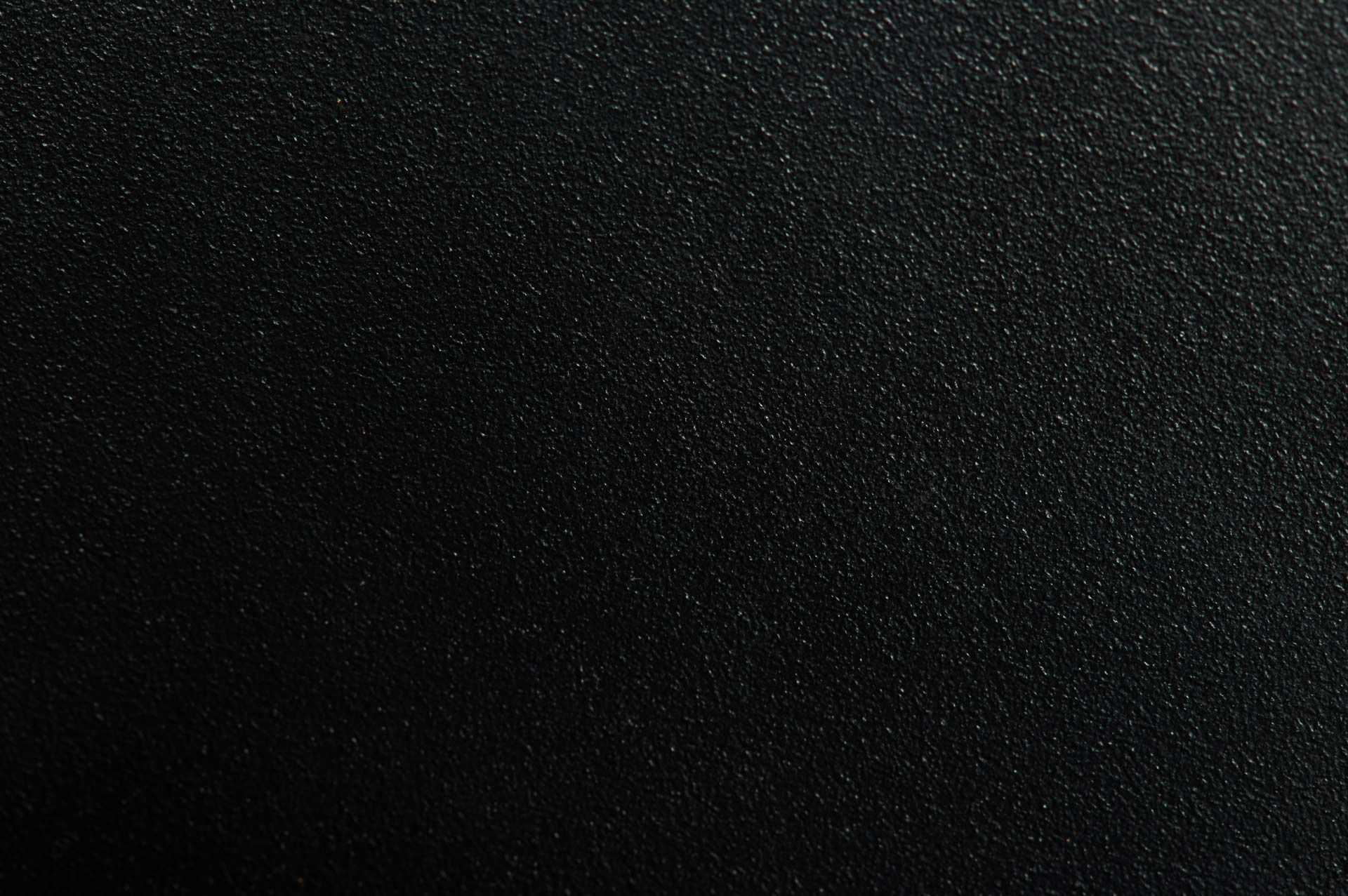 Gros plan sur une surface noire mate à la texture fine, mouchetée et granuleuse.