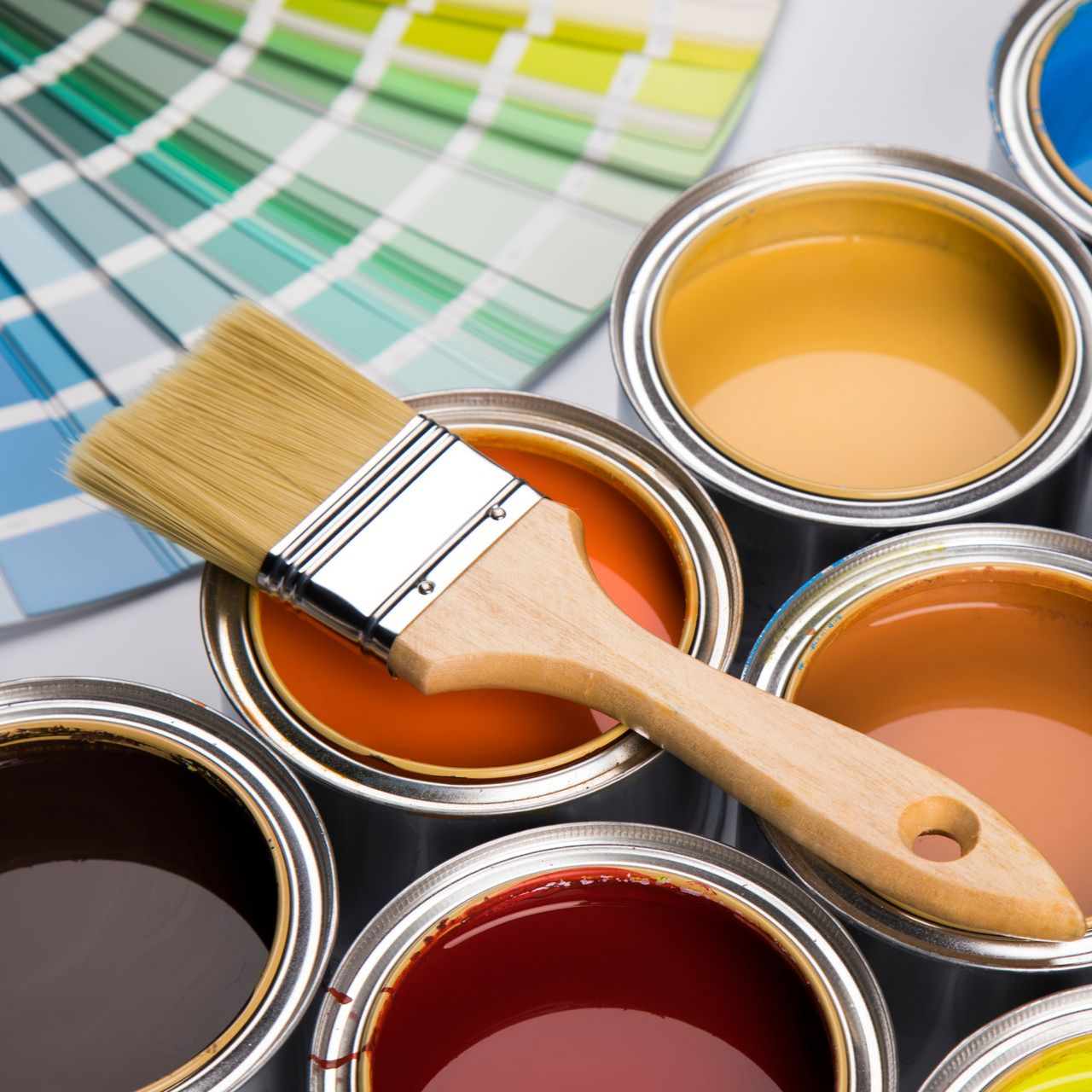 Un pinceau repose sur un pot de peinture orange ouvert, entouré d'autres pots de peinture et d'un éventail d'échantillons de couleurs.