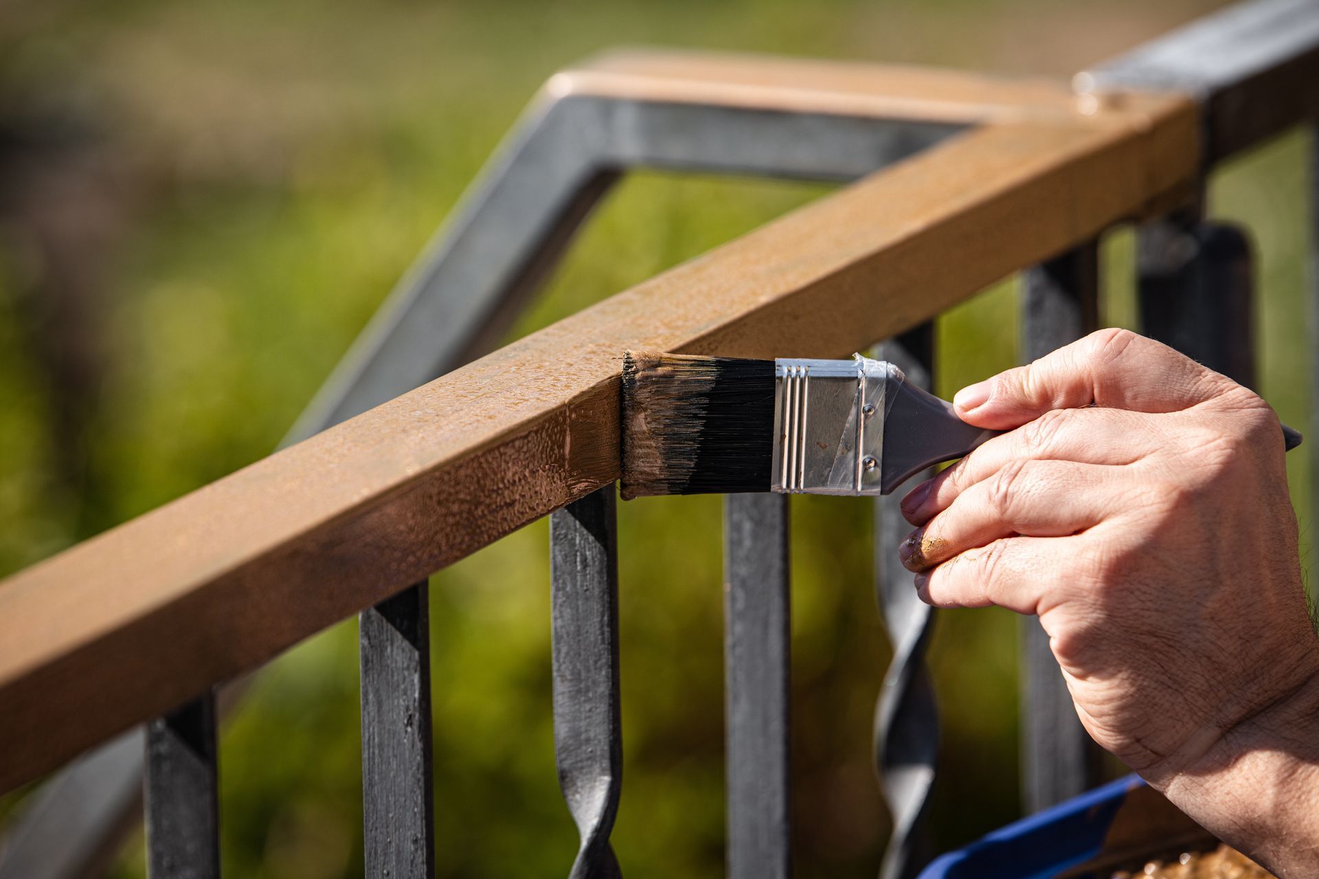 Une main tient un pinceau, teignant la traverse supérieure d'une balustrade métallique extérieure.