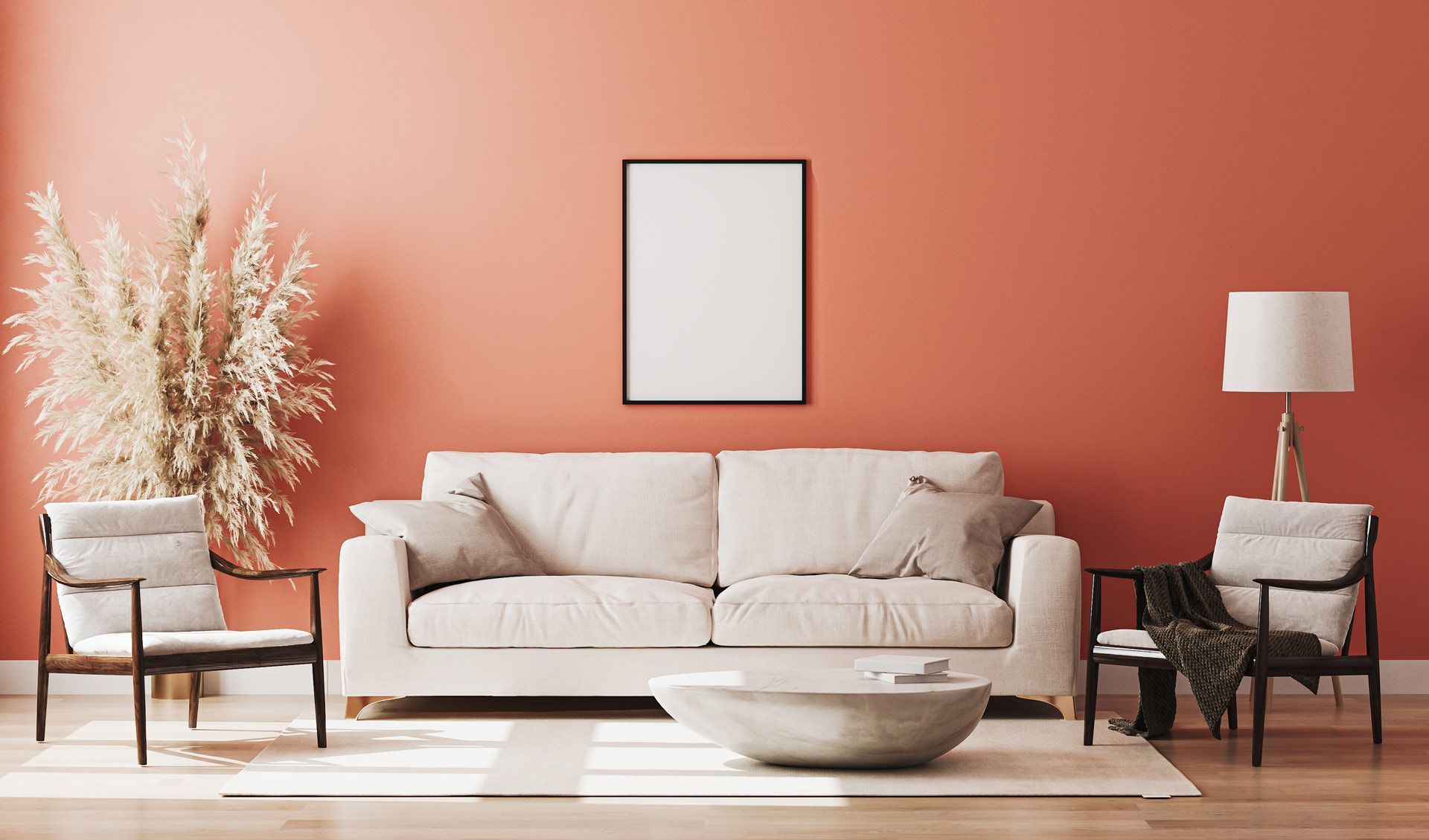 Un canapé beige flanqué de deux fauteuils, un lampadaire et une grande plante contre un mur corail avec un cadre photo vierge.