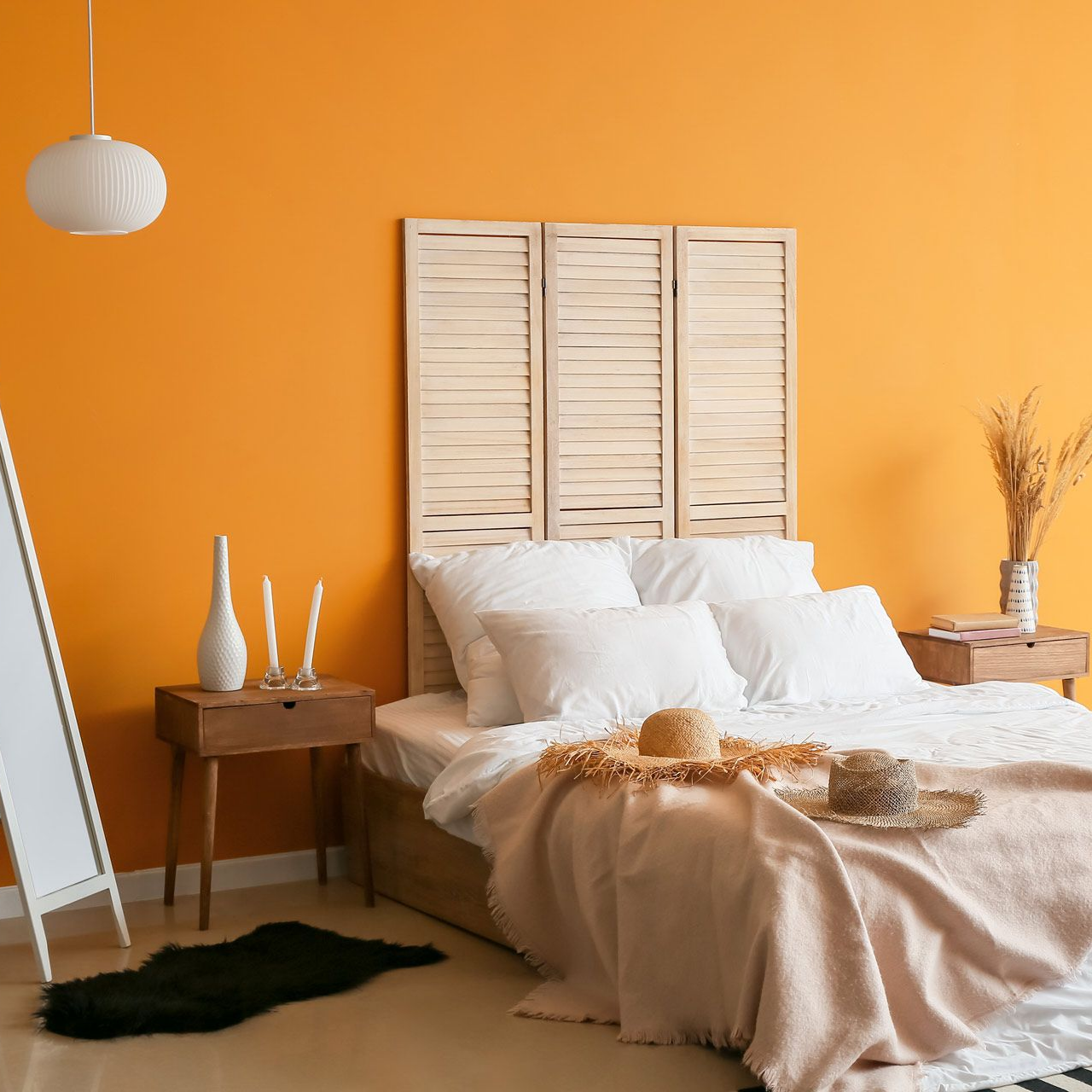 Une chambre confortable avec un mur d'accent orange, une tête de lit à lattes en bois, du linge de lit blanc et deux chapeaux de paille sur le lit.