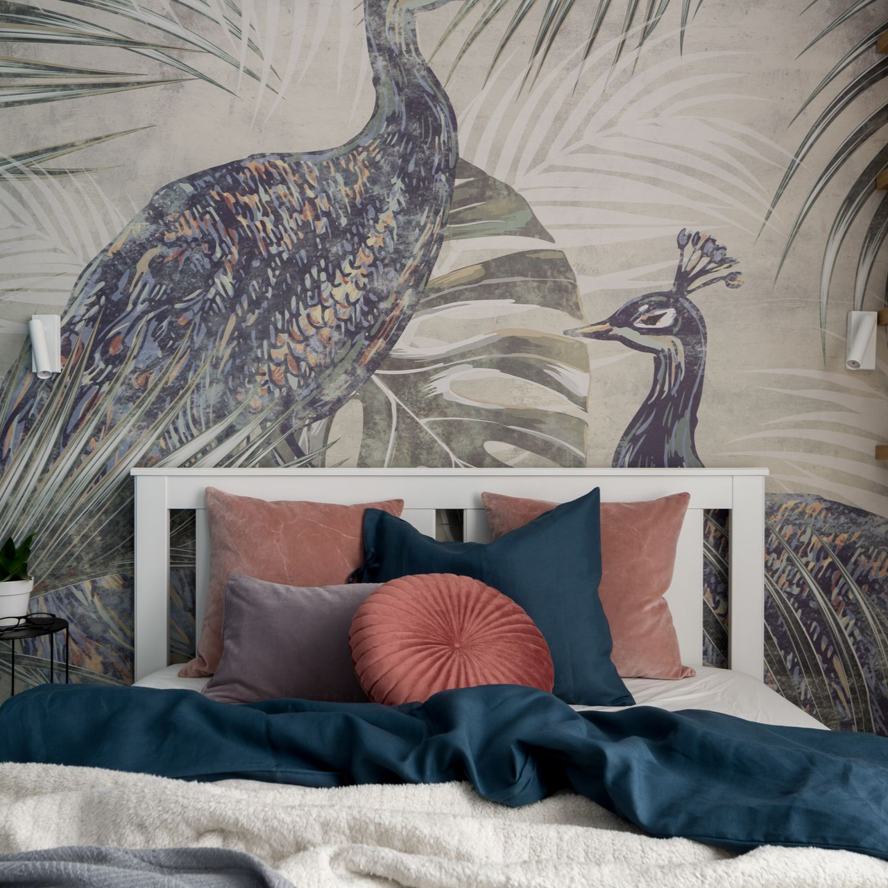Un lit avec des draps bleus et des coussins mauves, sur un papier peint panoramique représentant deux paons parmi des feuilles de palmier.