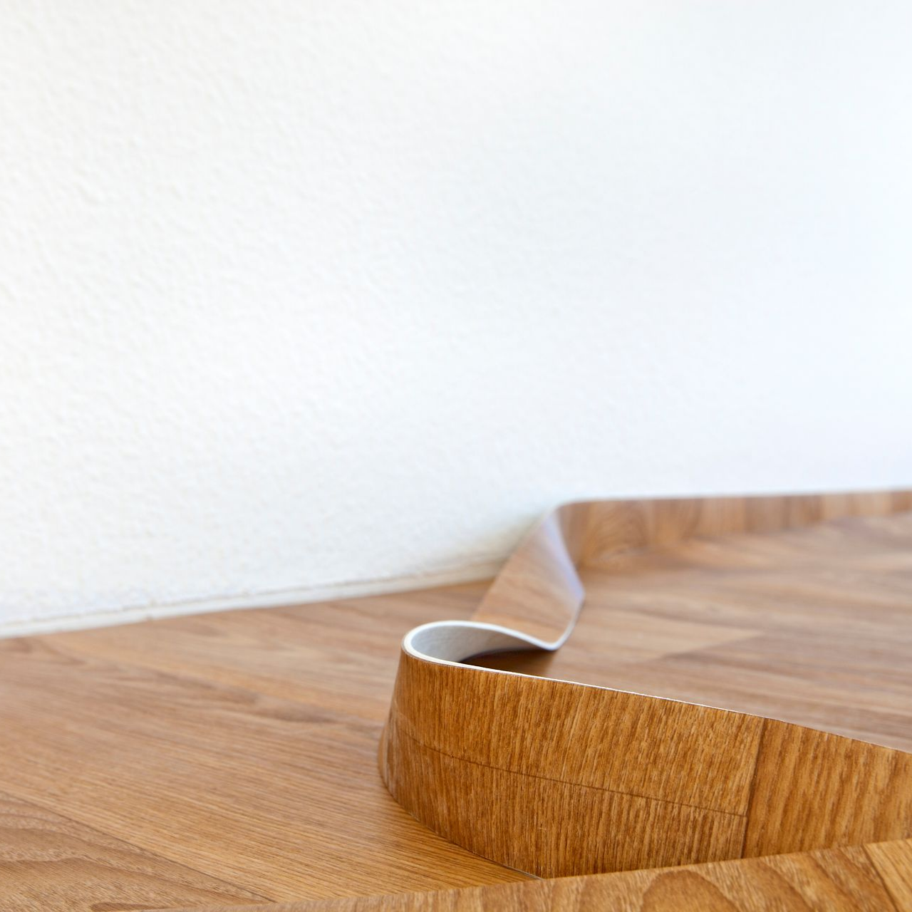 Une section de revêtement de sol en vinyle à motif bois se soulève et se décolle du mur.