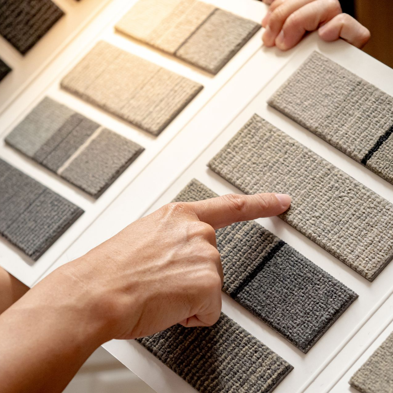 Une personne montrant du doigt un échantillon de moquette aux tons neutres dans un catalogue de décoration.