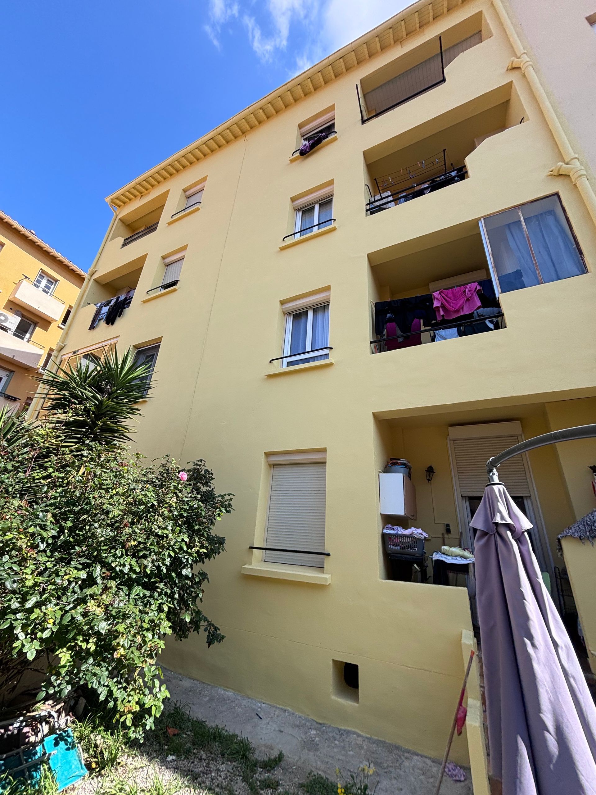 Vue en contreplongée d'un immeuble d'appartements jaune clair à plusieurs étages, avec balcons, fenêtres et linge étendu.