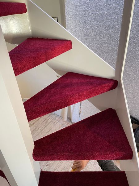 Un escalier en colimaçon aux cadres blancs et aux marches recouvertes d'une moquette texturée rouge vif.