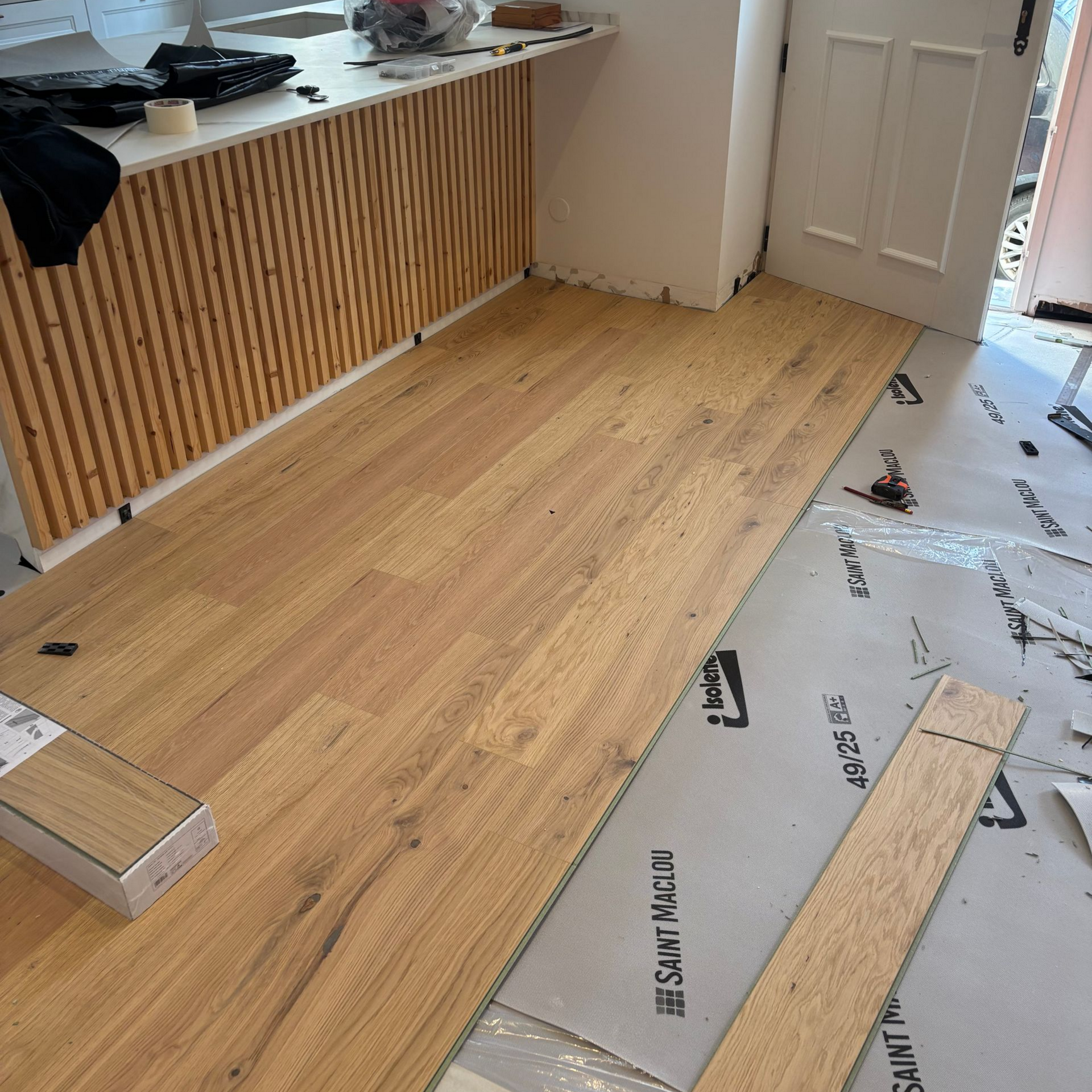 Un salon minimaliste baigné de lumière, avec un parquet à larges lattes, de hauts plafonds, de grandes fenêtres blanches et un canapé bas gris.