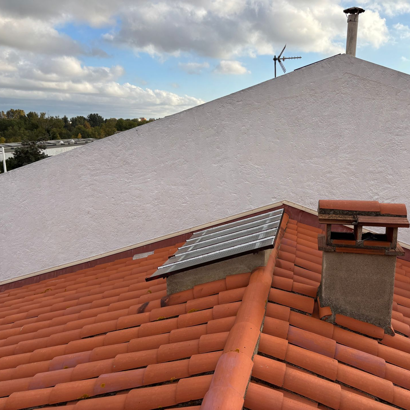 Une personne nettoie à haute pression des tuiles de toit en terre cuite orange, en éliminant la saleté sombre et la mousse.