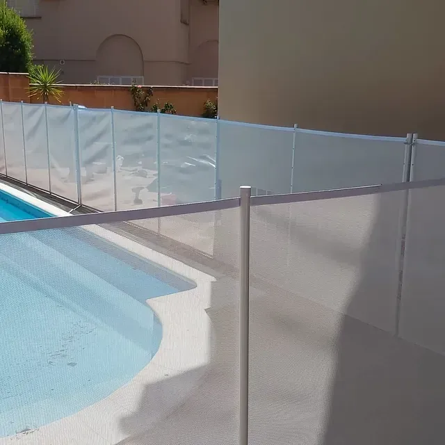 Una valla rodea una piscina con un edificio al fondo.