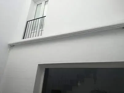 Una pared blanca con un balcón y una ventana.