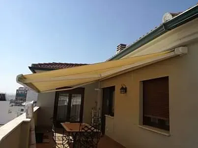 Un balcón con una mesa y sillas debajo de un toldo en el techo de un edificio.