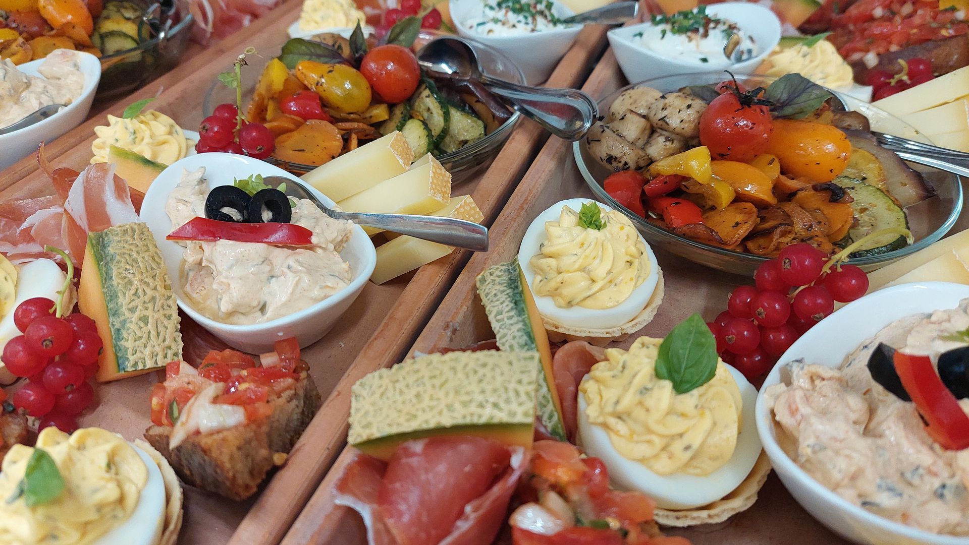 Buffettisch mit verschiedenen Vorspeisen, darunter kleine Sandwiches und Salate, in einem Raum mit Fenster.