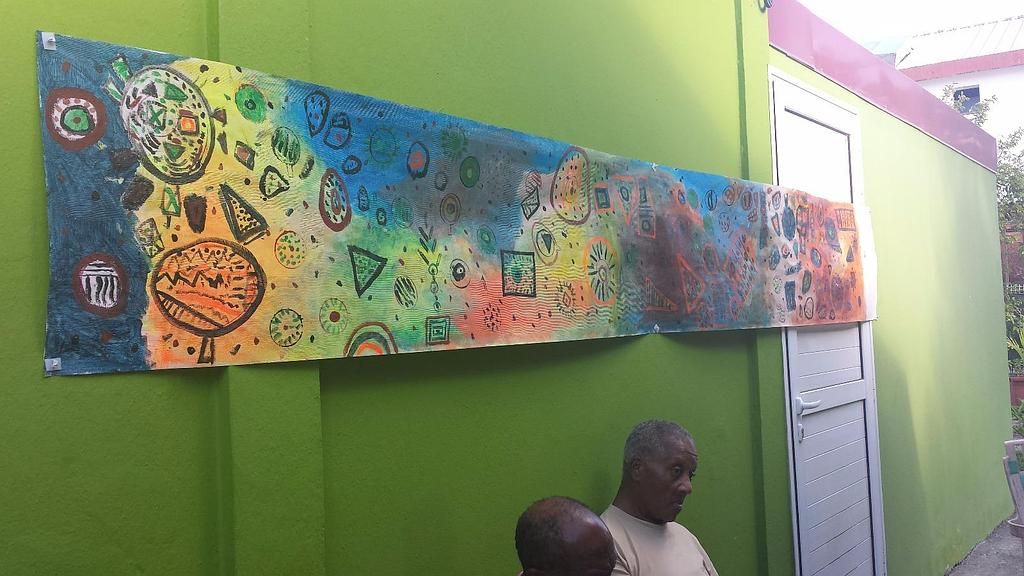 Fresque colorée peinte sur un mur vert, au-dessus de deux personnes assises dans une pièce.
