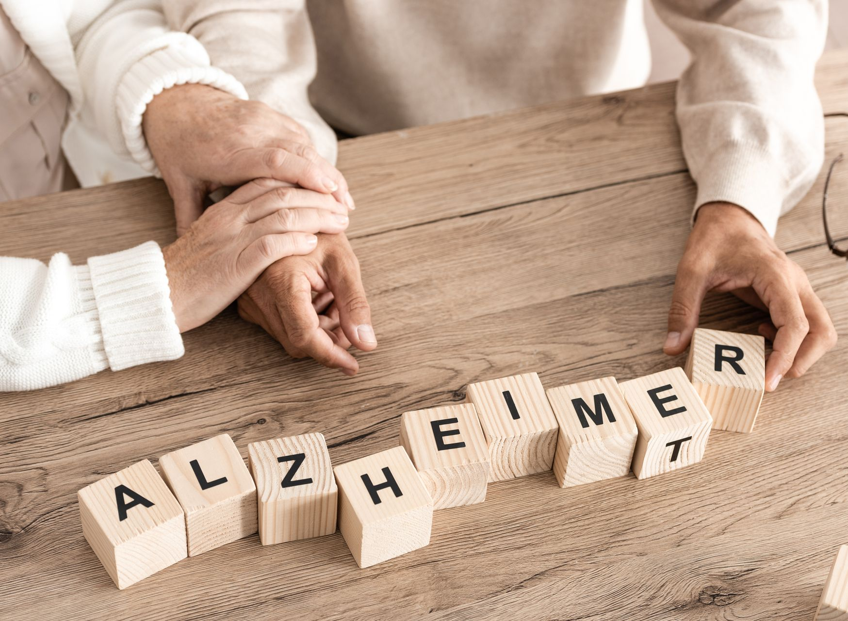 Des mains qui se tiennent au-dessus de lettres en bois formant le mot alzheimer