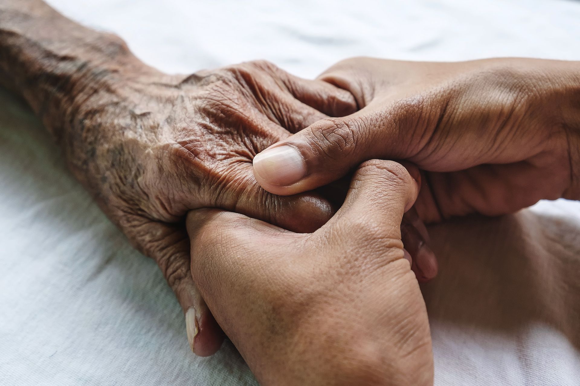 Des mains jointes dans un geste réconfortant sur la main d’une personne âgée.