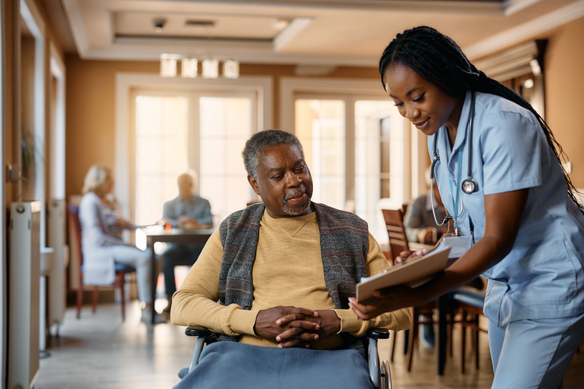 Une infirmière montre des documents à un patient assis dans le couloir lumineux d’un établissement de soins.